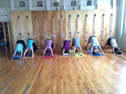 Students using the rope wall in downward facing dog in order to hold longer and give spine traction.