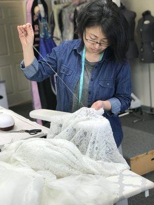 Sue hand sewing the final details of a lace wedding gown.