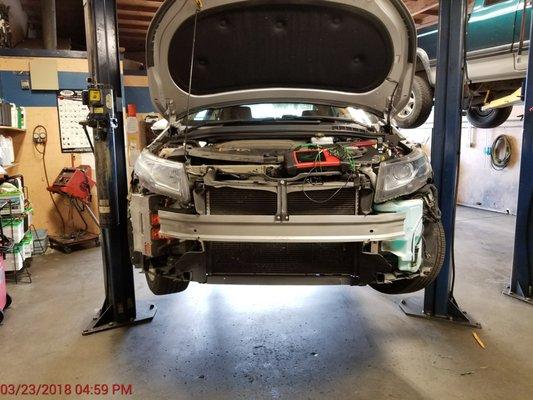 14 Volt w/front bumper cover removed to access PCM. HV battery charger can be seen on right side front corner. PCM on left front corner.