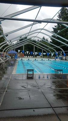 Outdoor swimming pool.  Notice it's raining, and the only cover is for the lifeguards.   Photo taken in mid-June.