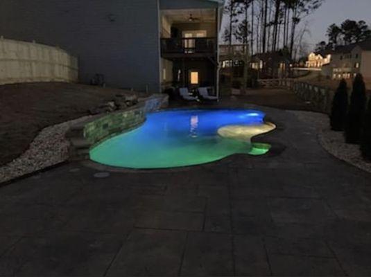 18'x34' freeform pool with sun shelf and swimout. Water feature wall with stacked stone. LED underwater lights. Stamped concrete. Tahoe Blue