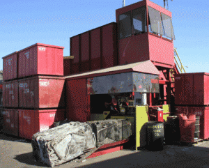 Stacked bins of scrap metal and actively baling material on site at Modesto Junk Company