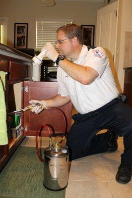 Spraying the back of a cabinet for pest control.